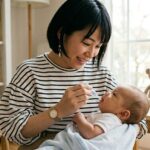 森のこどもクリニック（小児科・皮膚科）のロゴが入ったアイキャッチ画像。明るい室内で、ストライプのシャツを着た母親が赤ちゃんを抱き、笑顔でスポイトを使ってK2シロップを飲ませている。テーブルにはK2シロップの瓶とテディベア、カゴがあり、背景の本棚には『子育てのヒント』や『赤ちゃんの基本』といった育児書が並んでいる。